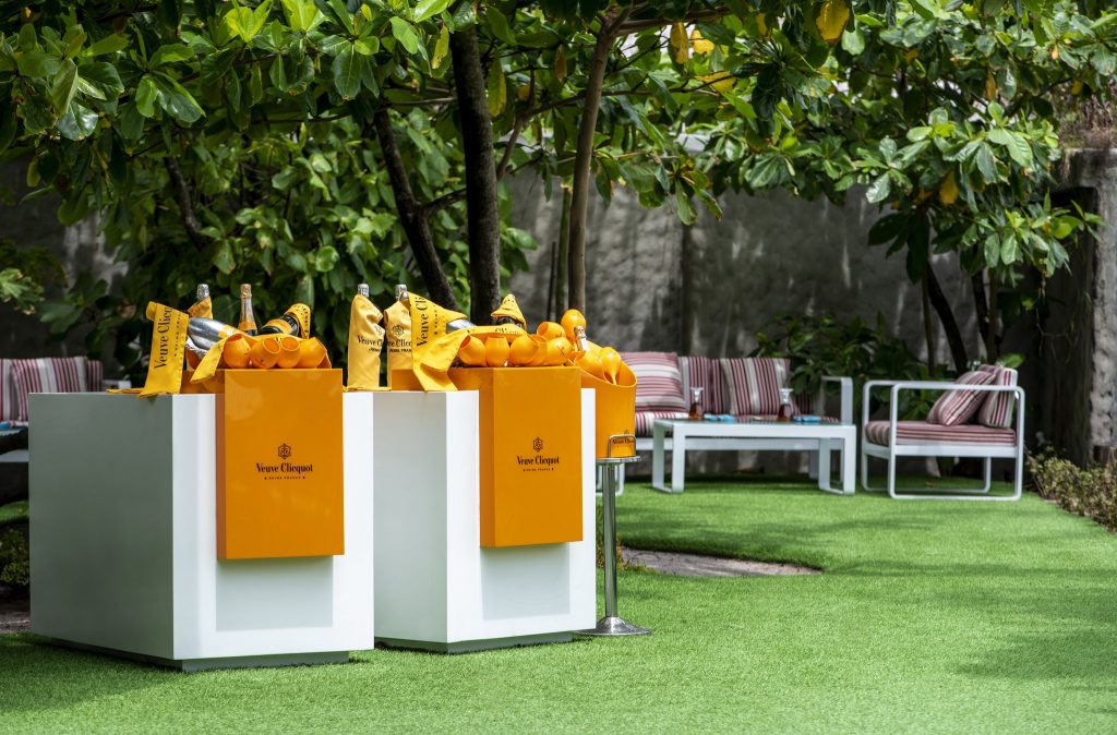 Außenbereich mit grünem Rasen, weißen kubischen Tischen und orangen Veuve Clicquot Accessoires im You & Me Maldives.