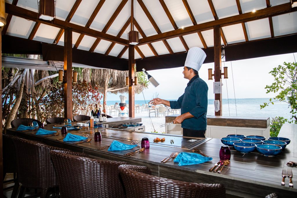 Offener Restaurantbereich You & Me Maldives Restaurant Rising Sun mit Koch, Holzbalken, Strohdach und Meer im Hintergrund