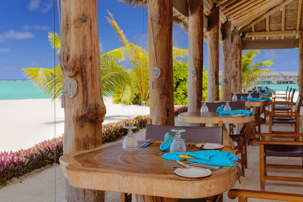 Offenes Restaurant The Sand mit Holzmöbeln, türkisfarbenen Servietten und Meerblick auf den