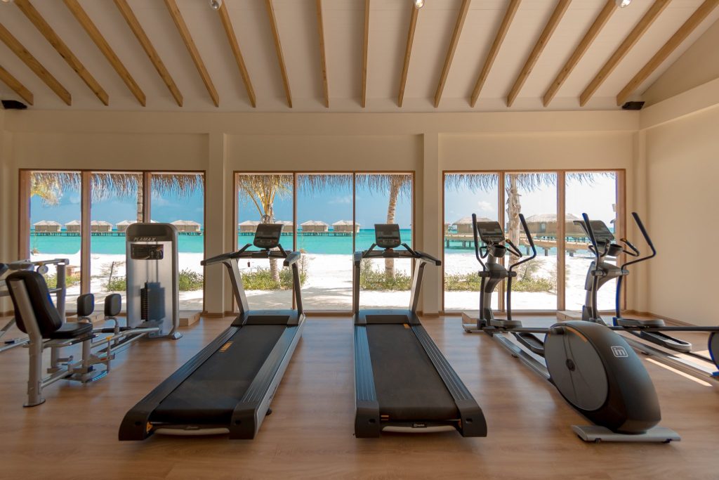 Moderner Fitnessraum mit Laufbändern und großen Fenstern zum weißen Sandstrand auf den
