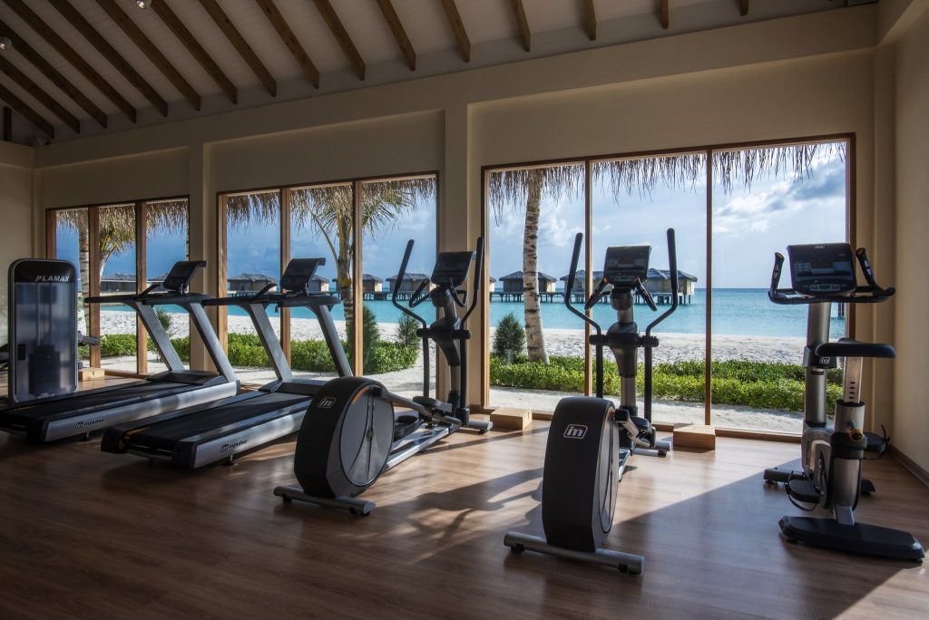 Moderner Fitnessraum mit Laufbändern und Ellipsentrainern, großen Fenstern und Meerblick im You & Me Maldives