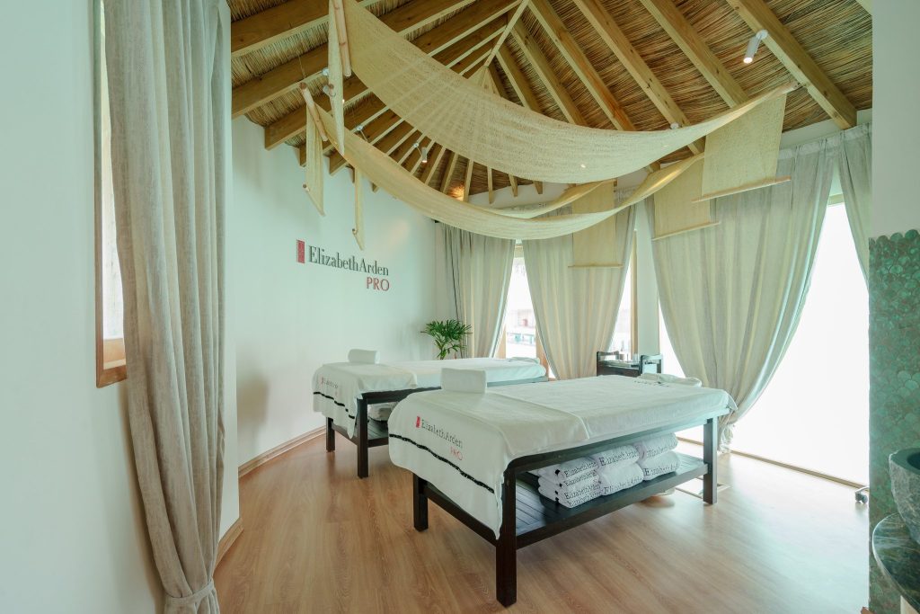 Spa-Raum im You & Me Maldives mit zwei weißen Massageliegen, Holzdecke und beigen Vorhängen