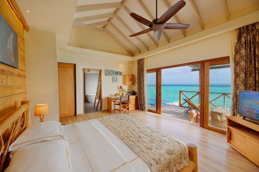 Geräumiges Aqua Suite Zimmer mit hellem Holz, großen Glasschiebetüren und Blick auf das türkisfarbene Meer