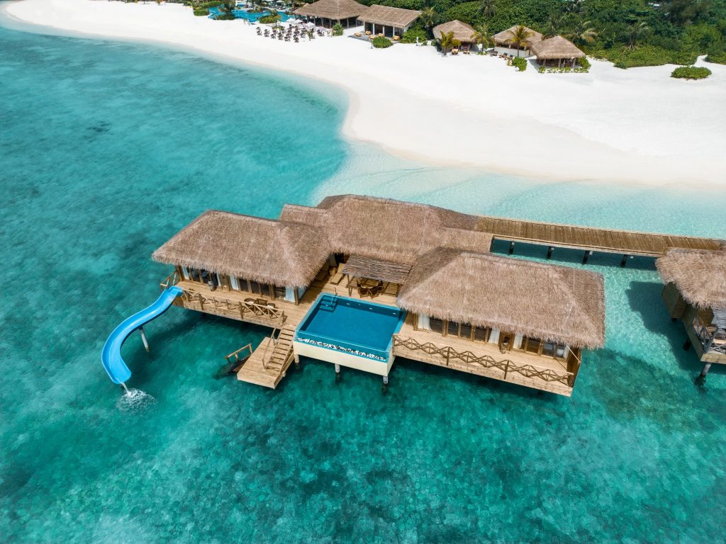 Überwasser-Villa You & Me Suite mit Holzbau, Strohdach, Pool und blauer Wasserrutsche ins türkisfarbene Meer
