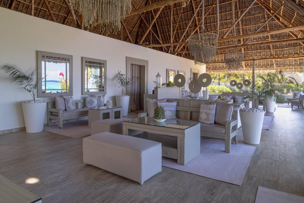 Barbereich im Zawadi Hotel mit gepolsterten Sofas, Holzboden, Glas-Tischen und geflochtener Holzdecke