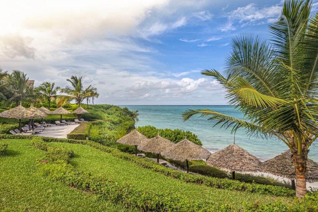 Strandliegen aus Holz und Stoff unter strohgedeckten Sonnenschirmen am Meer im Zawadi Hotel Sansibar
