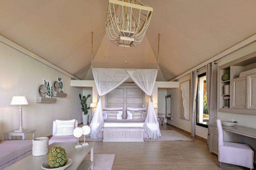 Helles Hotelzimmer der Private Villa im Zawadi Hotel mit Himmelbett, Holzfußboden und Pflanzenbildern an der Wand