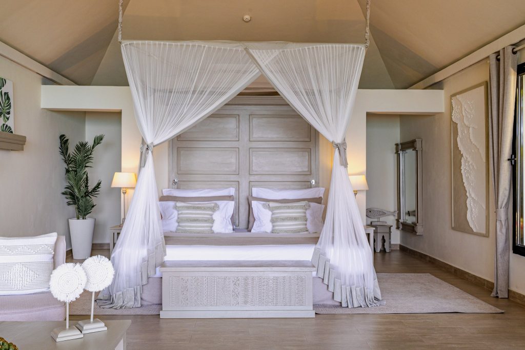 Hotelzimmer im Zawadi Hotel mit Himmelbett, Sitzgelegenheit, großen Fenstern und hellen Vorhängen