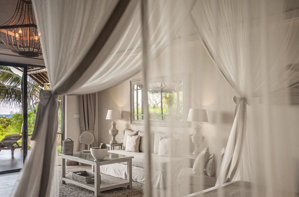 Helles Hotelzimmer im Zawadi Hotel mit Holz-Kronleuchter, weißen Möbeln und Blick auf tropischen Garten in Sansibar