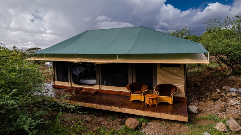Zeltähnliches Gebäude auf Holzplattform mit zwei Rattanstühlen und kleinem Tisch auf Veranda, grüne und beige Farbtöne