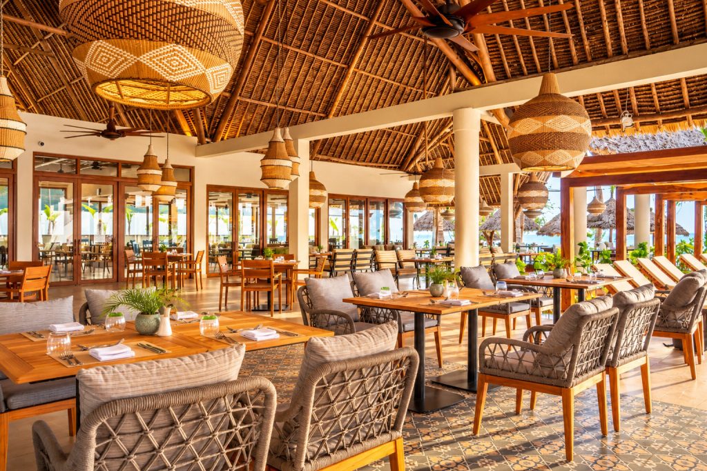 Offener Restaurantbereich im JAZ Elite Adonia mit Holztischen, gepolsterten Stühlen und hängenden tropischen Pflanzen