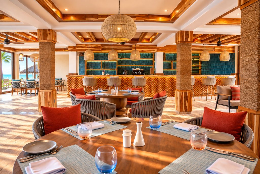 Restaurant im JAZ Elite Adonia mit runden Holztischen, geflochtenen Stühlen, großen Lampen und Meerblick