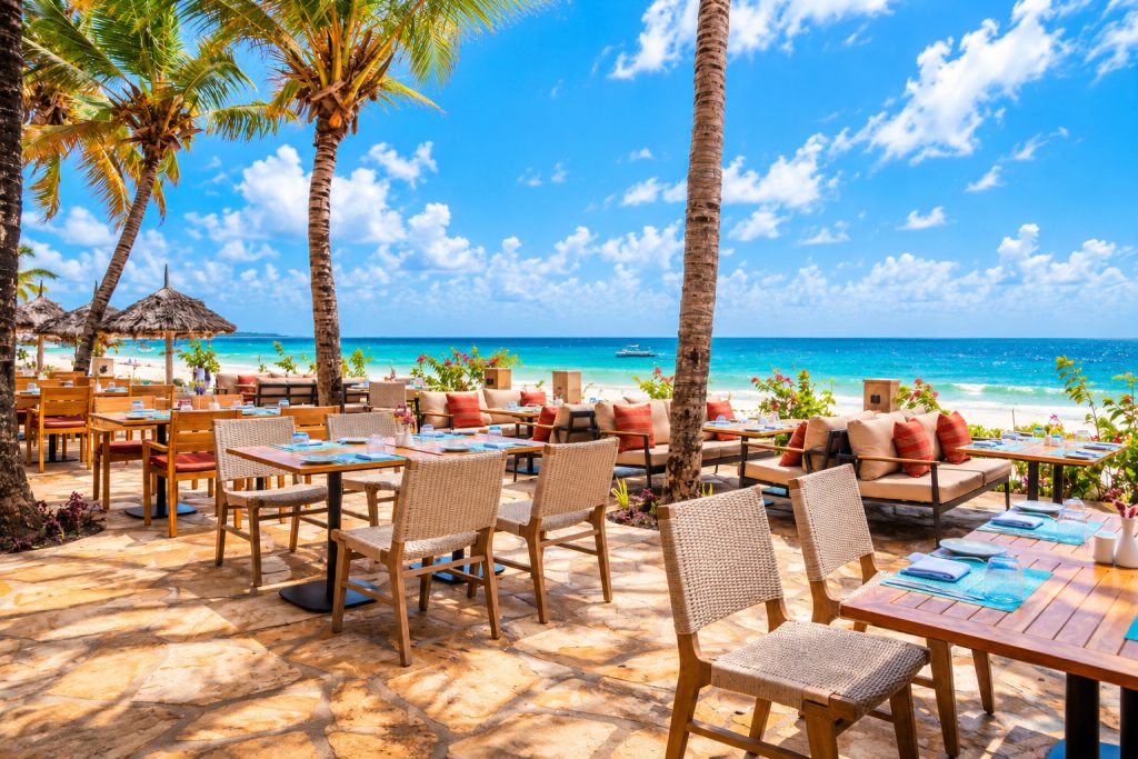 Strandterrasse im JAZ Elite Adonia mit Holz- und Rattanmöbeln unter Palmen und Meerblick