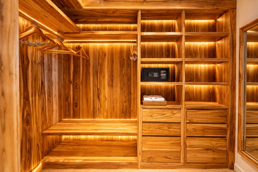 Begehbarer Kleiderschrank mit Holzregalen, Holzbügeln, schwarzem Safe und Korb mit weißen Handtüchern