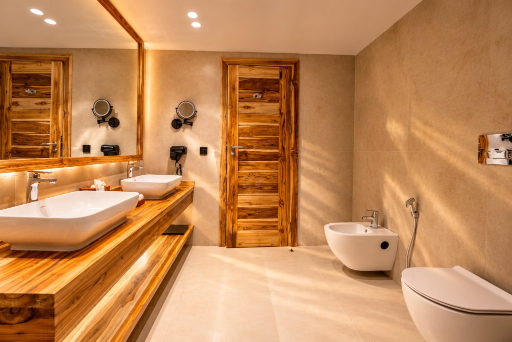 Modernes Badezimmer mit Holzwaschtisch, großem Spiegel und beigen Fliesen im JAZ Elite Adonia Sansibar