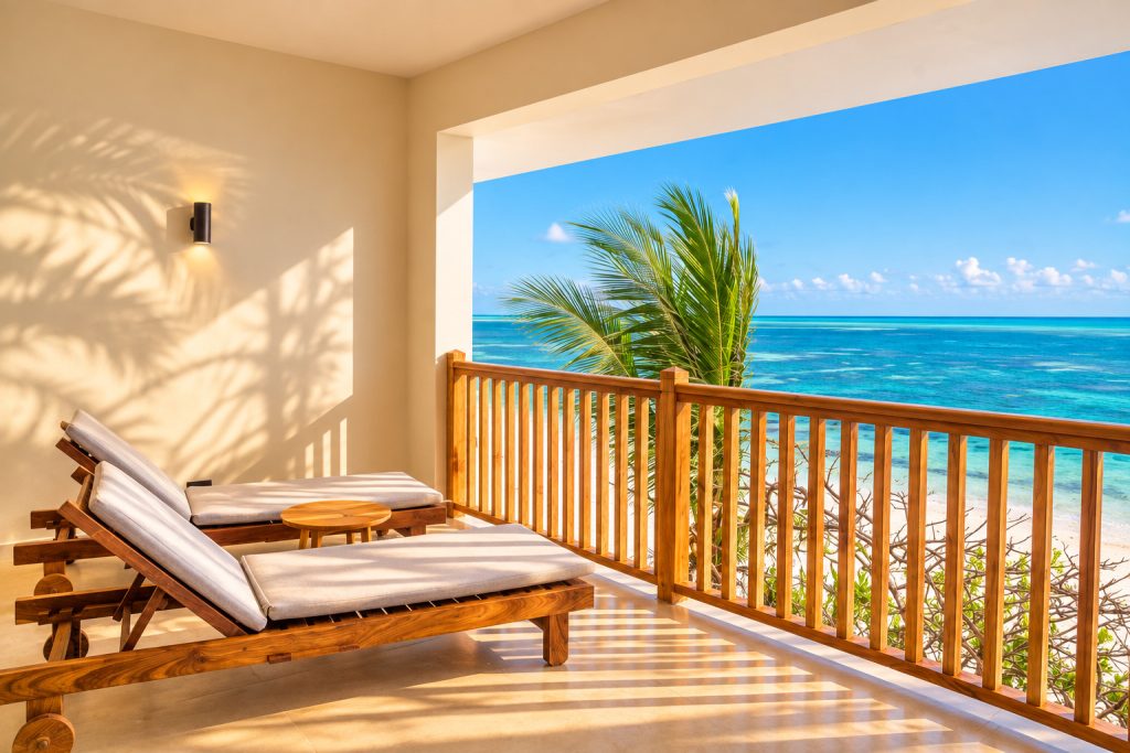Balkon mit zwei Holzliegestühlen, Beistelltisch und Blick auf blauen Ozean und Sandstrand im Deluxe Ocean Front View Room