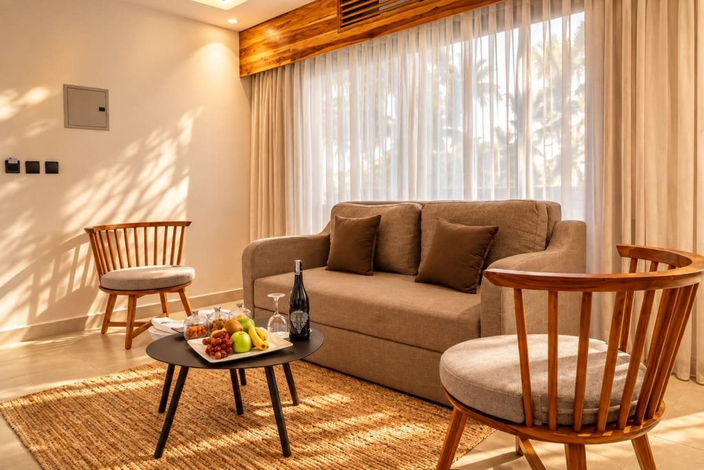 Beige Zweisitzer-Sofa mit zwei Holzsesseln und rundem Couchtisch mit Früchten