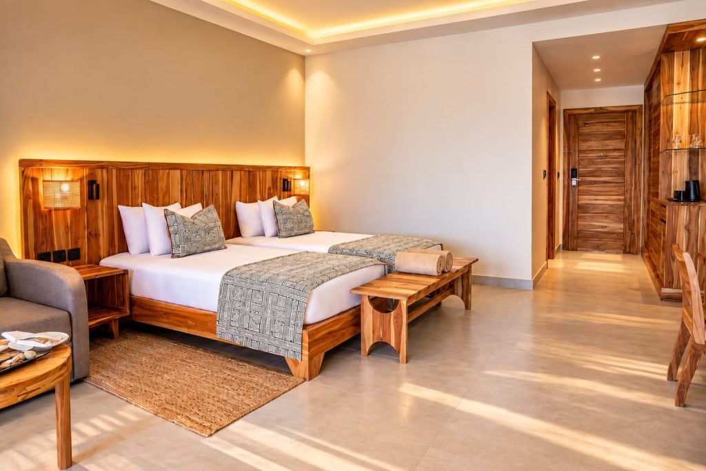 Hotelzimmer mit zwei Betten, warmen Holztönen, weißen Laken und grauen Überwürfen im Premium Deluxe Pool View Room