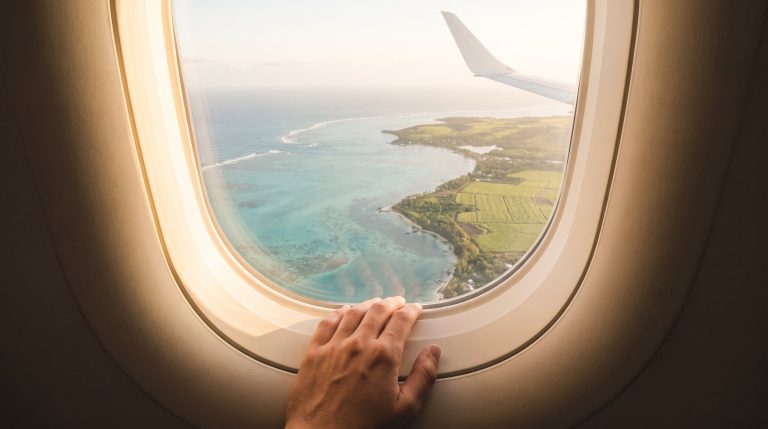 Blick aus dem Flugzeugfenster auf die gruene Kueste von Mauritius waehrend des Anflugs