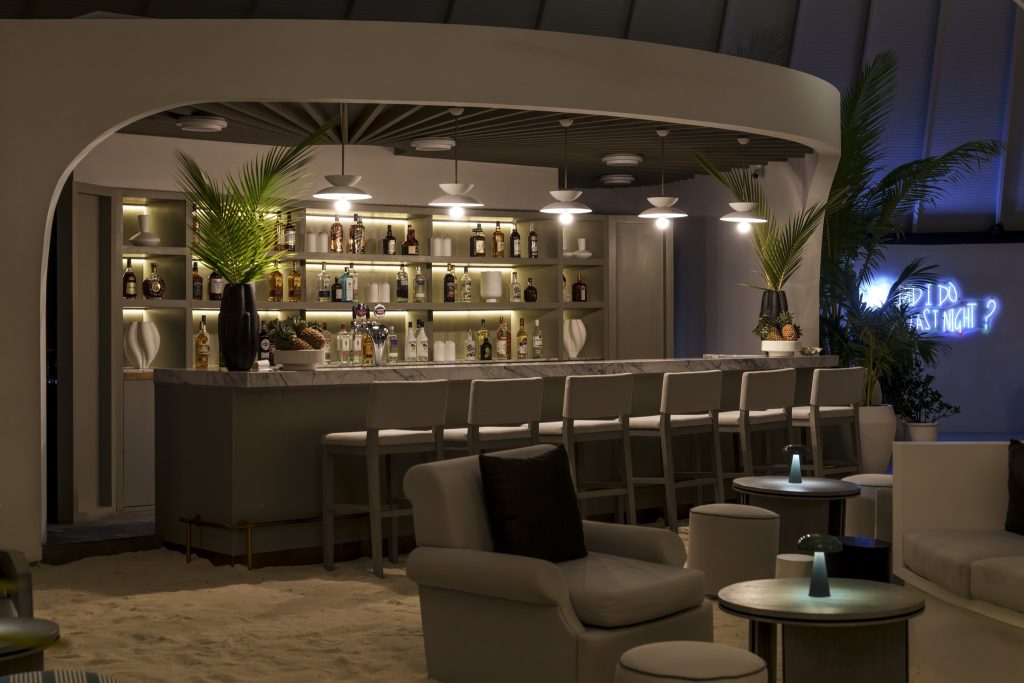 Bar Nautilus im Sun Siyam Vilu Reef mit Marmortheke, Holzbarhockern, Sesseln und neonblauem Schriftzug