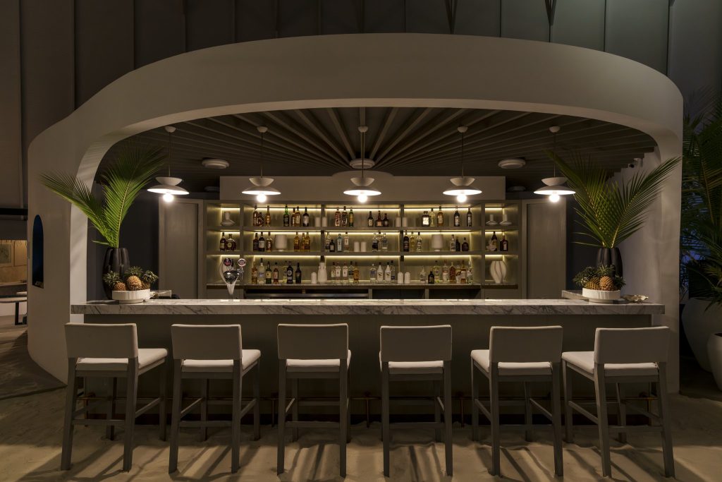 Bar Nautilus im Sun Siyam Vilu Reef mit sechs hohen Holzbarstühlen, Marmorbar und beleuchteten Regalen