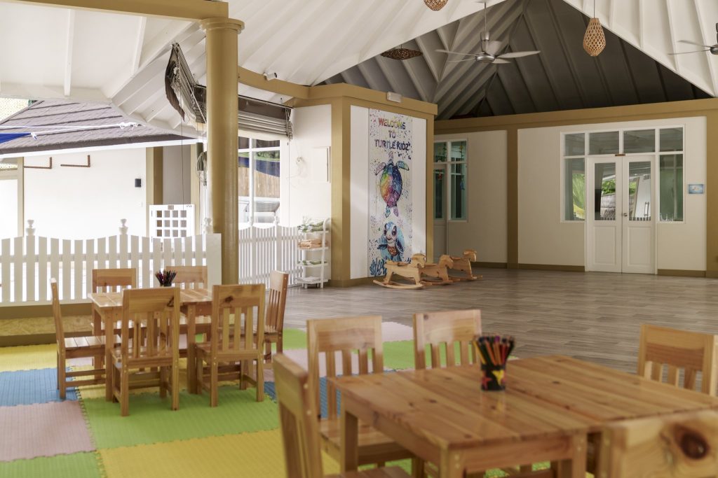 Kinderraum im Sun Siyam Vilu Reef mit Holztischen, bunten Bodenmatten, Wandbild und geflochtenen Deckenlampen