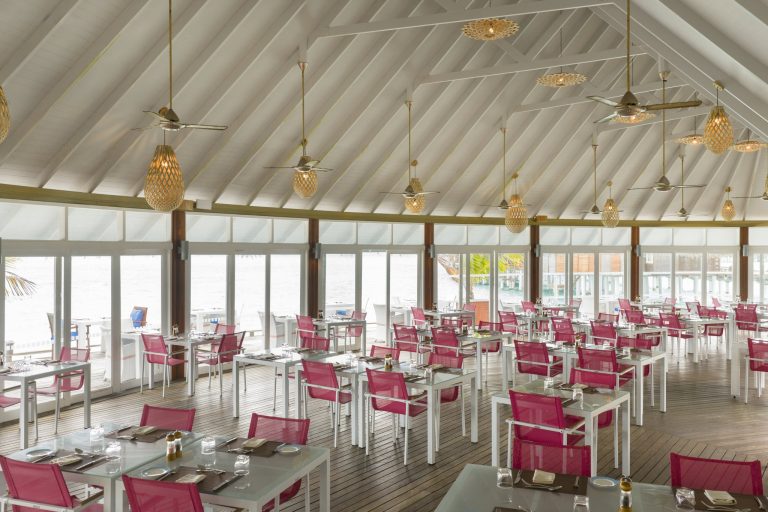 Geräumiges Restaurant Aqua im Sun Siyam Vilu Reef mit rosafarbenen Stühlen, Glastischen und Blick aufs Wasser
