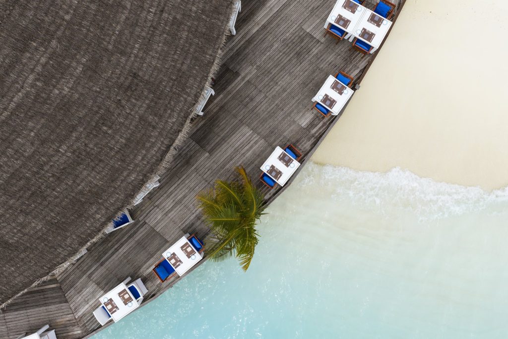 Vogelperspektive auf Restaurant Aqua Terrasse mit weißen Tischen und blauen Stühlen am Strand