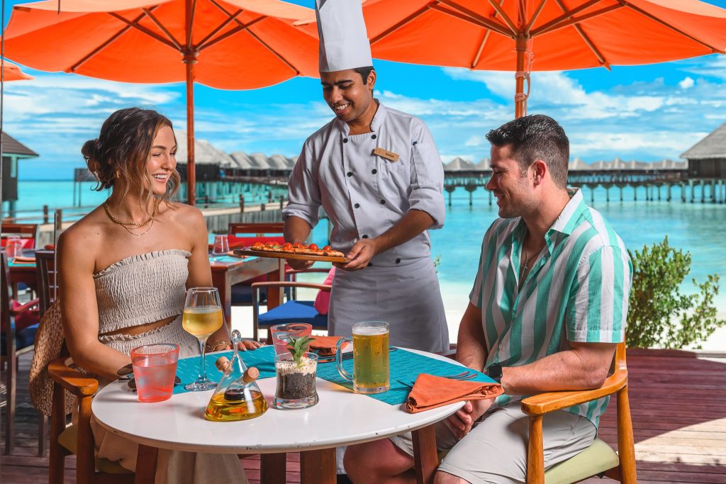 Terrassenszene im restaurant-spice-03 mit Gästen an rundem Tisch und Kellner im Sun Siyam Vilu Reef