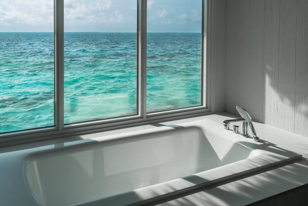 Weiße Badewanne aus Keramik mit Chromarmaturen vor großem Fenster mit Meerblick in 2BR Ocean Signature Villa