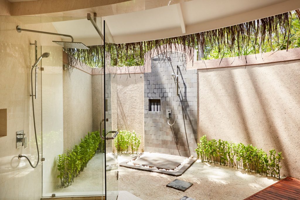Badezimmer mit offener Dusche, Glaswand, beigen Steinwänden und Holzdielen im Beach Villa with Pool