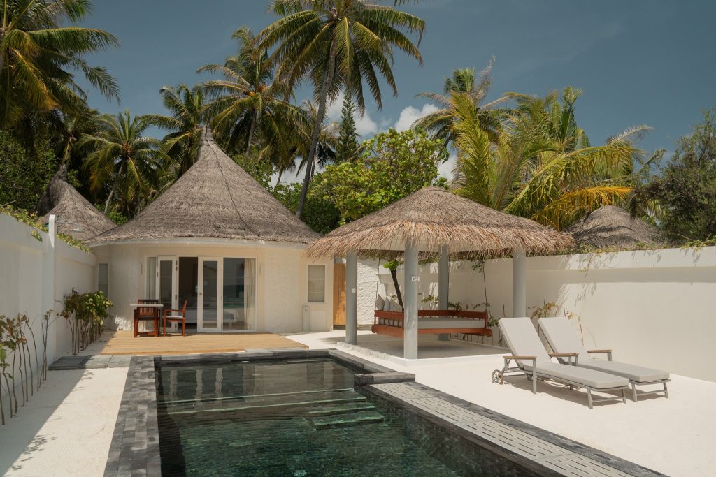 Rechteckiger Pool vor rundem Bungalow mit Stroh gedecktem Dach und Holzterrasse im Sun Siyam Vilu Reef