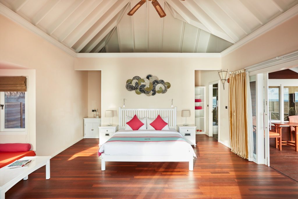 Helles Zimmer der Reef Villa im Sun Siyam Vilu Reef mit weißem Giebel-Dach, großem Bett und Balkon mit Holzmöbeln