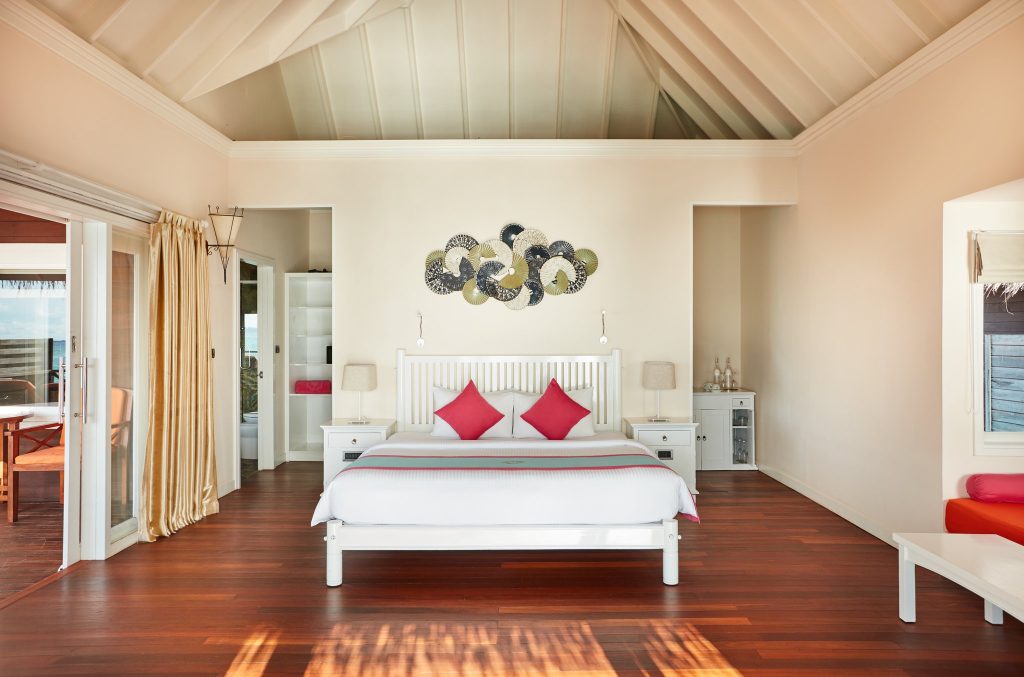 Geräumiges Zimmer der Sunset Reef Villa mit großem weißen Bett, rotem Sofa und offener Balkontür auf den