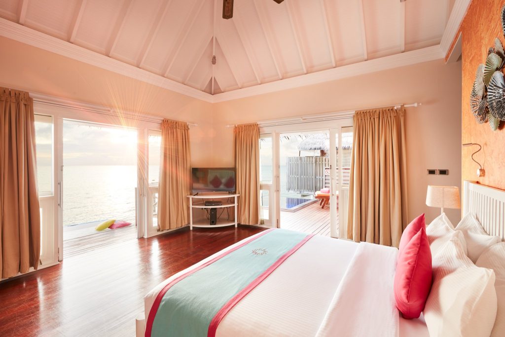 Helles Water Villa Zimmer mit großem Bett, Meerblick, Terrasse, Holzfußboden und großen Glasfenstern im Sun Siyam Vilu Reef